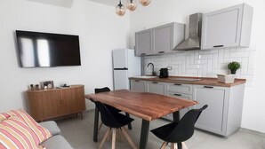 A modern kitchen with grey cabinets, a wooden dining table, black chairs, a grey sofa, and a TV mounted on the wall. - Domus Luxi - Teulada Design Apartment | Style and Comfort (Teulada)