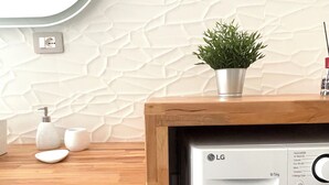 A modern laundry room with a washing machine, a small potted plant, and a wooden counter. - Domus Luxi - Teulada Design Apartment | Style and Comfort (Teulada)