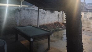 A billiards table under a shelter with a brick wall and a metal fence in the background. - Janete Hostel Ingleses  (Florianopolis)