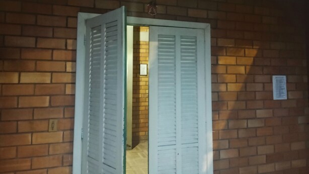 A doorway with white shutters, a brick wall, and a small sign on the right. - Janete Hostel Ingleses  (Florianopolis)