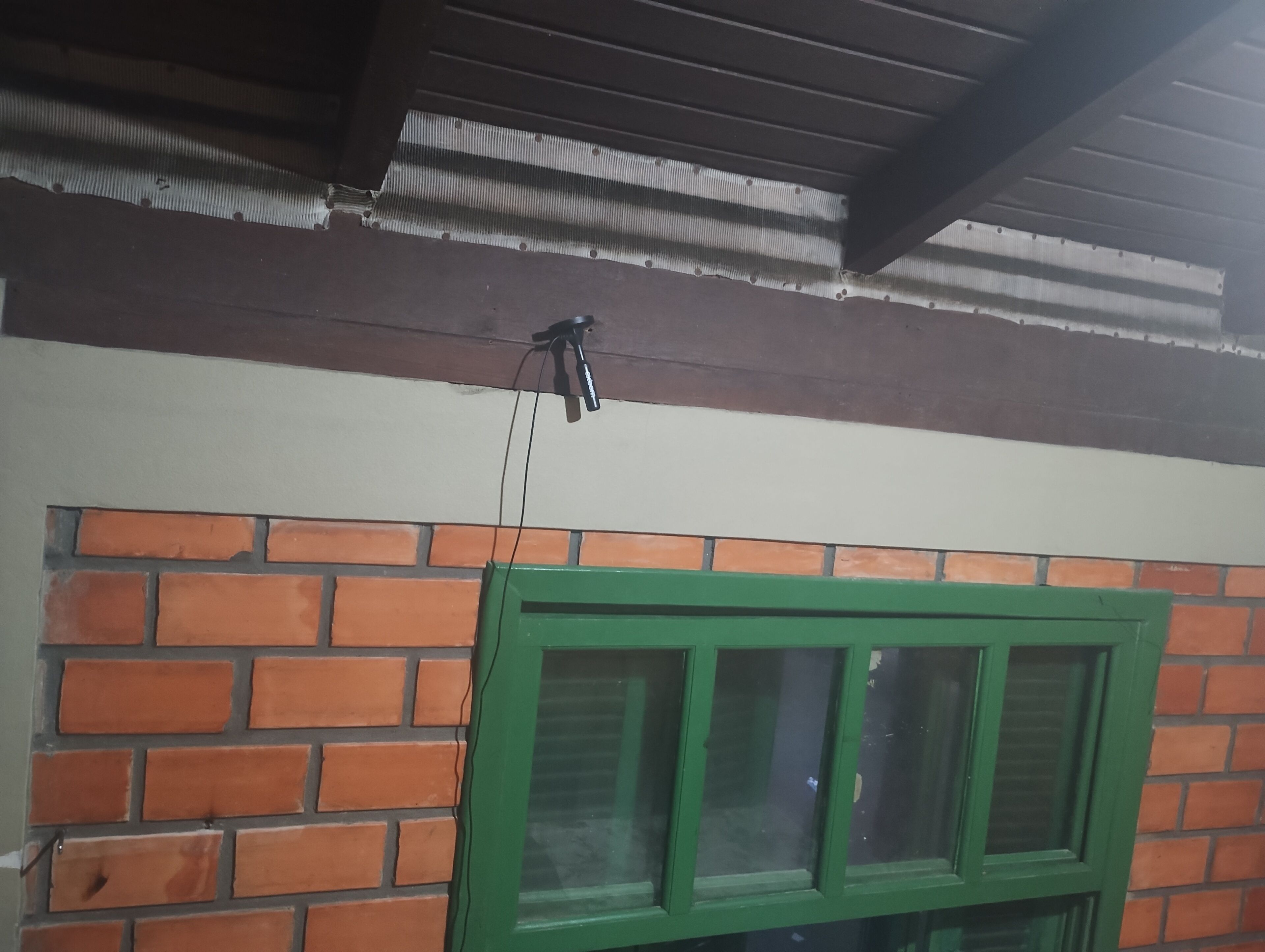 Un muro de ladrillo con una ventana de marco verde y un techo metálico.