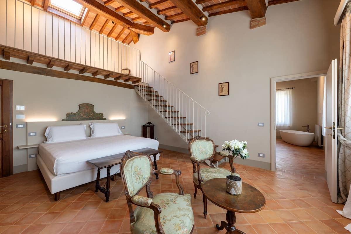 Une chambre avec un grand lit, un escalier en bois et un coin repas comprenant des chaises et une table.