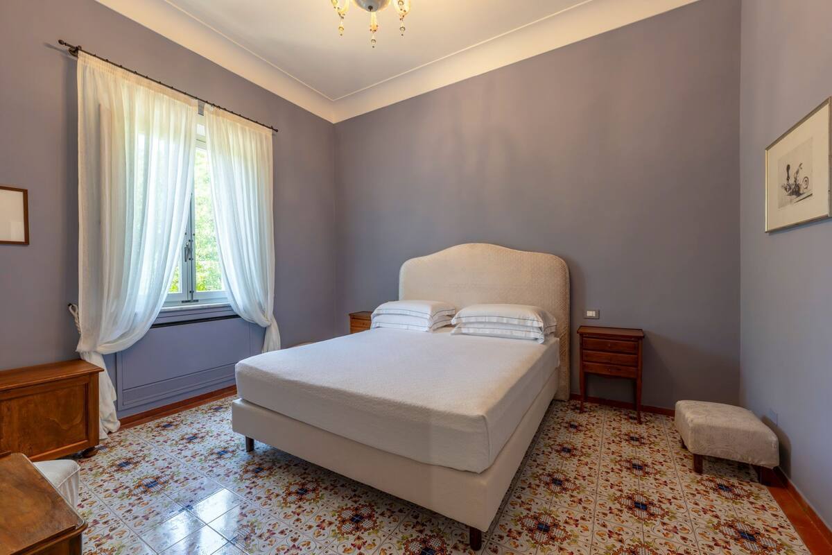 Une chambre à coucher avec un lit, une table de chevet, une chaise et une fenêtre avec des rideaux.