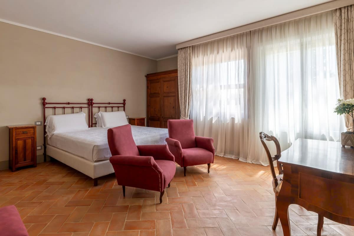 Une chambre à coucher comprenant un lit, deux fauteuils, une table de chevet en bois, une commode en bois, une table à manger et une plante en pot.