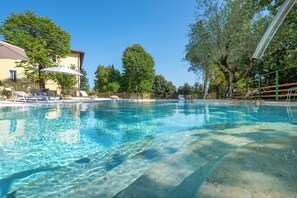 A clear swimming pool with lounge chairs and umbrellas, surrounded by trees and a building. - Nobilis Charme Relais (Montepulciano)