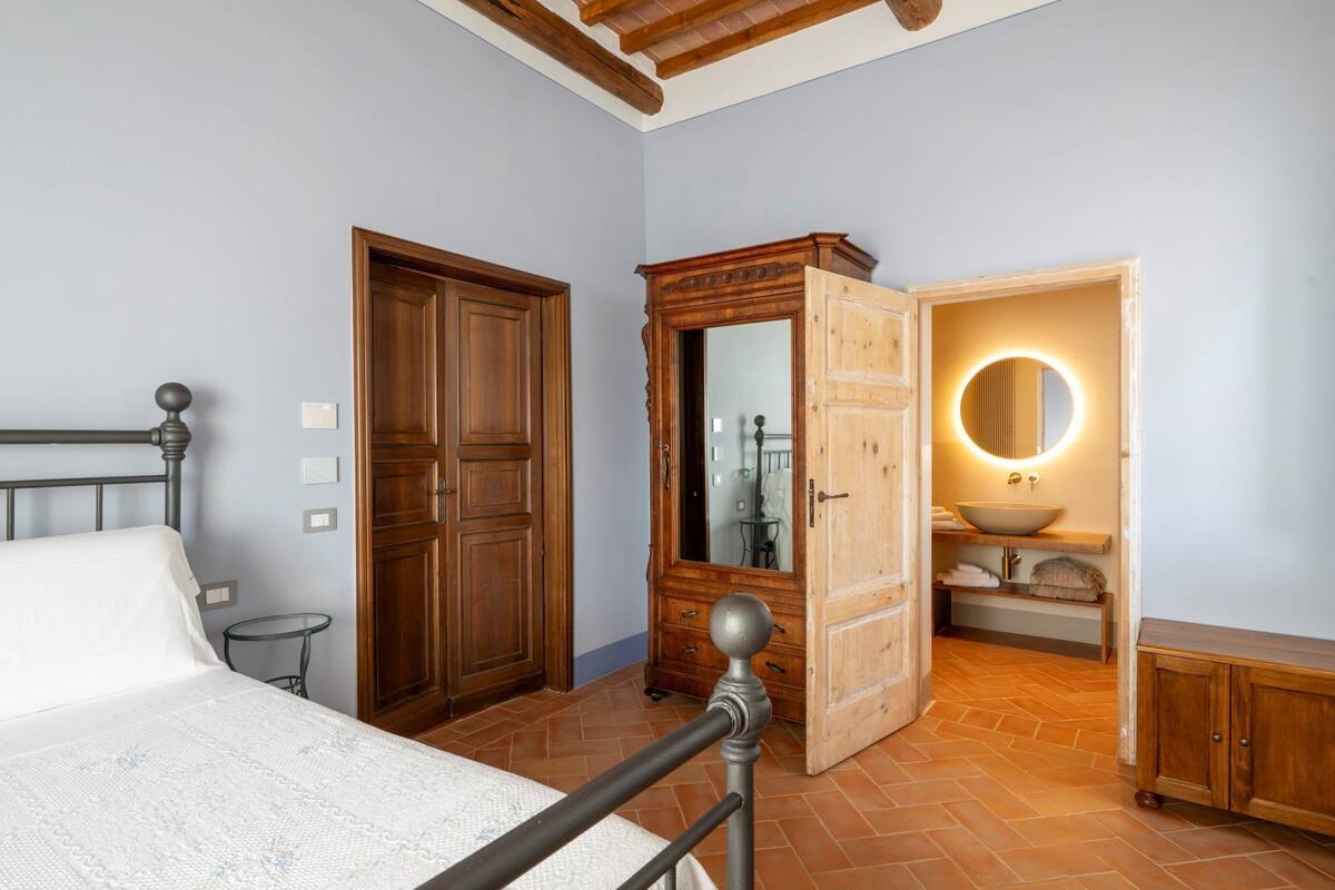 Une chambre à coucher avec un lit, une armoire en bois et une salle de bain dotée d’un miroir rond et d’un lavabo.