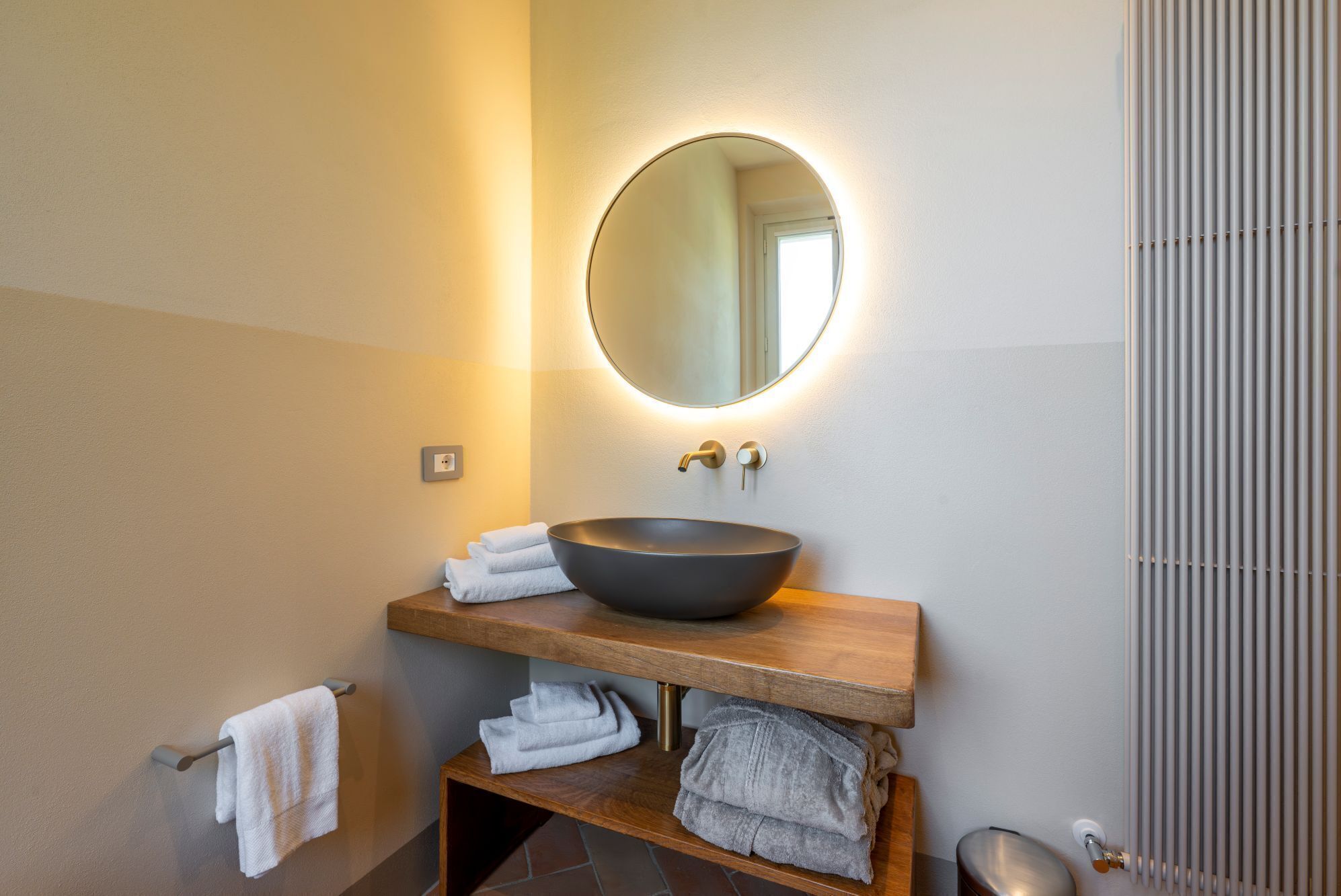 A modern bathroom with a round mirror, a vessel sink, and a wooden vanity.