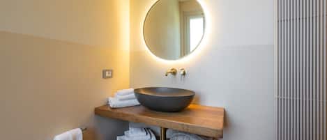 A modern bathroom with a round mirror, a vessel sink, and a wooden vanity.