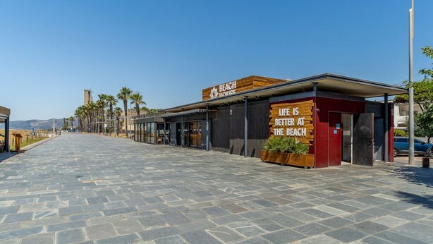 Un immeuble situé en bord de mer, avec une enseigne indiquant « MAISON DE PLAGE » et un slogan : « LA VIE EST PLUS BELLE À LA PLAGE ».