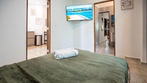 A hotel room with a bed, a TV on the wall, and a view of the beach through the window.