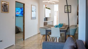 A modern living room with a gray sofa, a dining area with a table set for six, and a kitchen visible through an open doorway.
