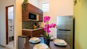 A modern kitchen with a microwave, stainless steel refrigerator, and a dining table set with plates and a potted orchid.