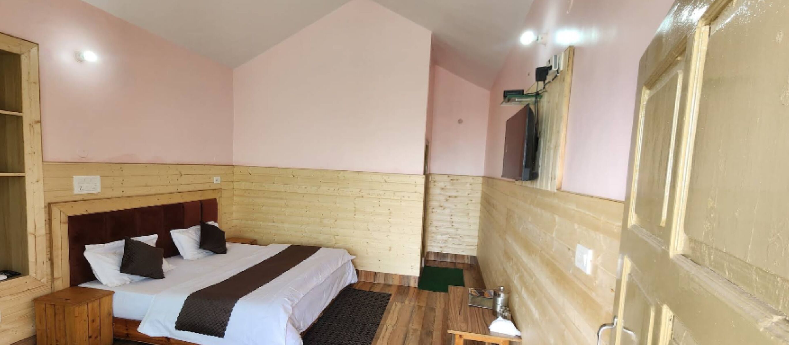 A bedroom with a wooden headboard, a bed with white bedding and a dark brown throw, a wooden nightstand, and a small wooden stool.