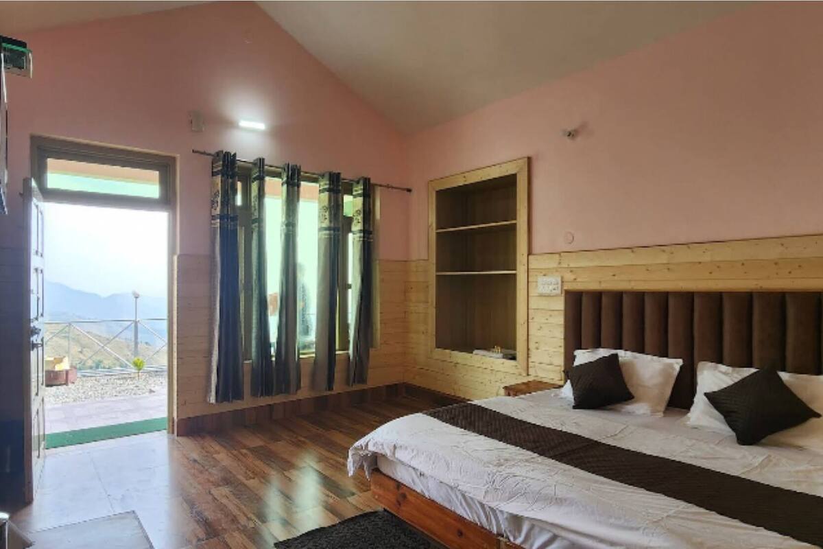 Une chambre à coucher avec un lit, une tête de lit en bois, une fenêtre avec des rideaux et une porte donnant sur un espace extérieur.