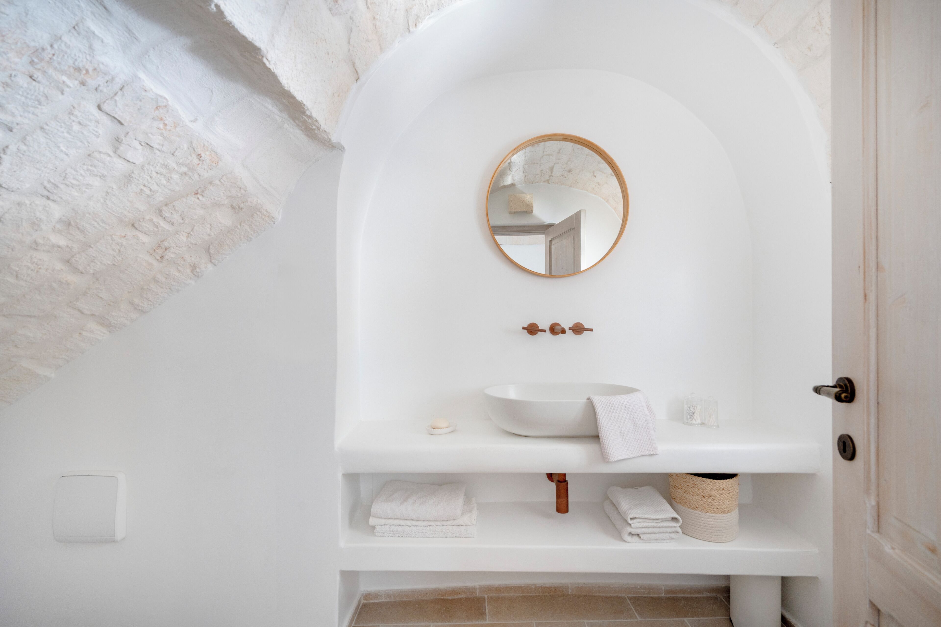 Een witte badkamer met een ronde spiegel, een wit wastafelmeubel en een handdoekrek.