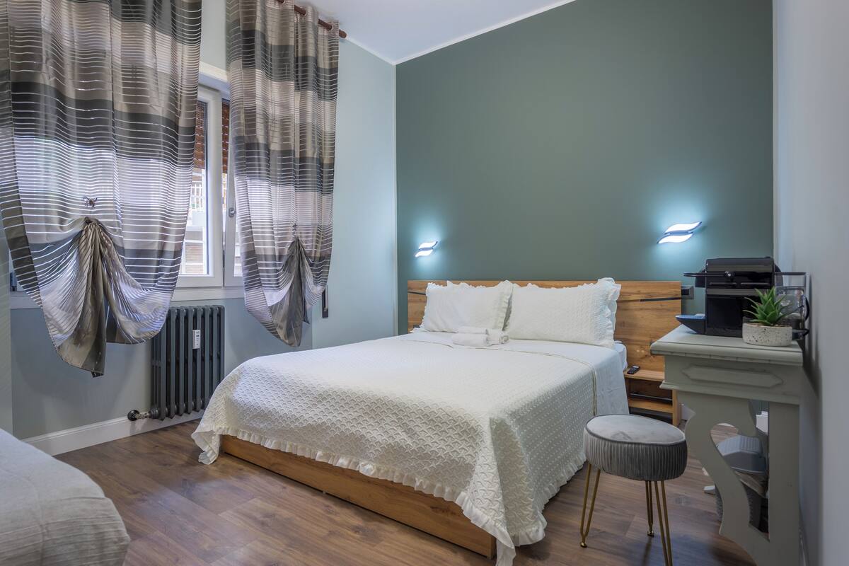 A neatly arranged bedroom with a wooden bed, a bedside table with a lamp, and a small stool.