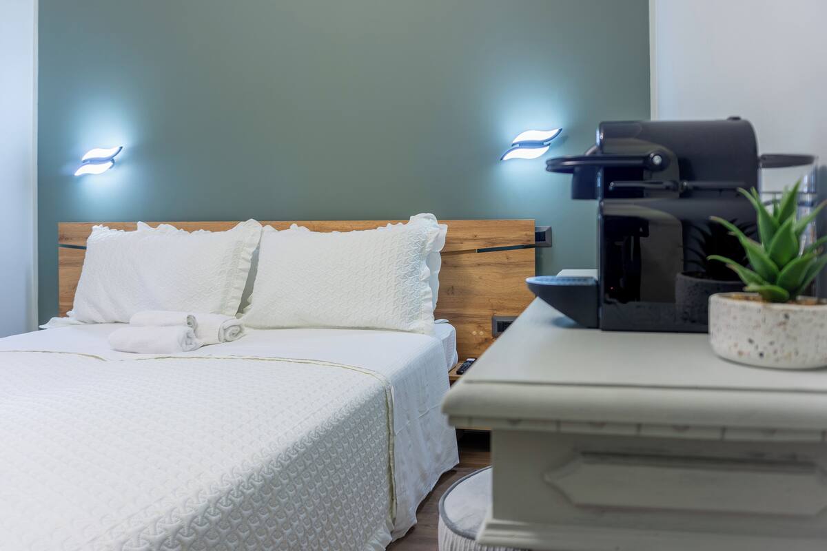 A neatly made bed with a wooden headboard, a coffee machine, and a small potted plant on a bedside table.