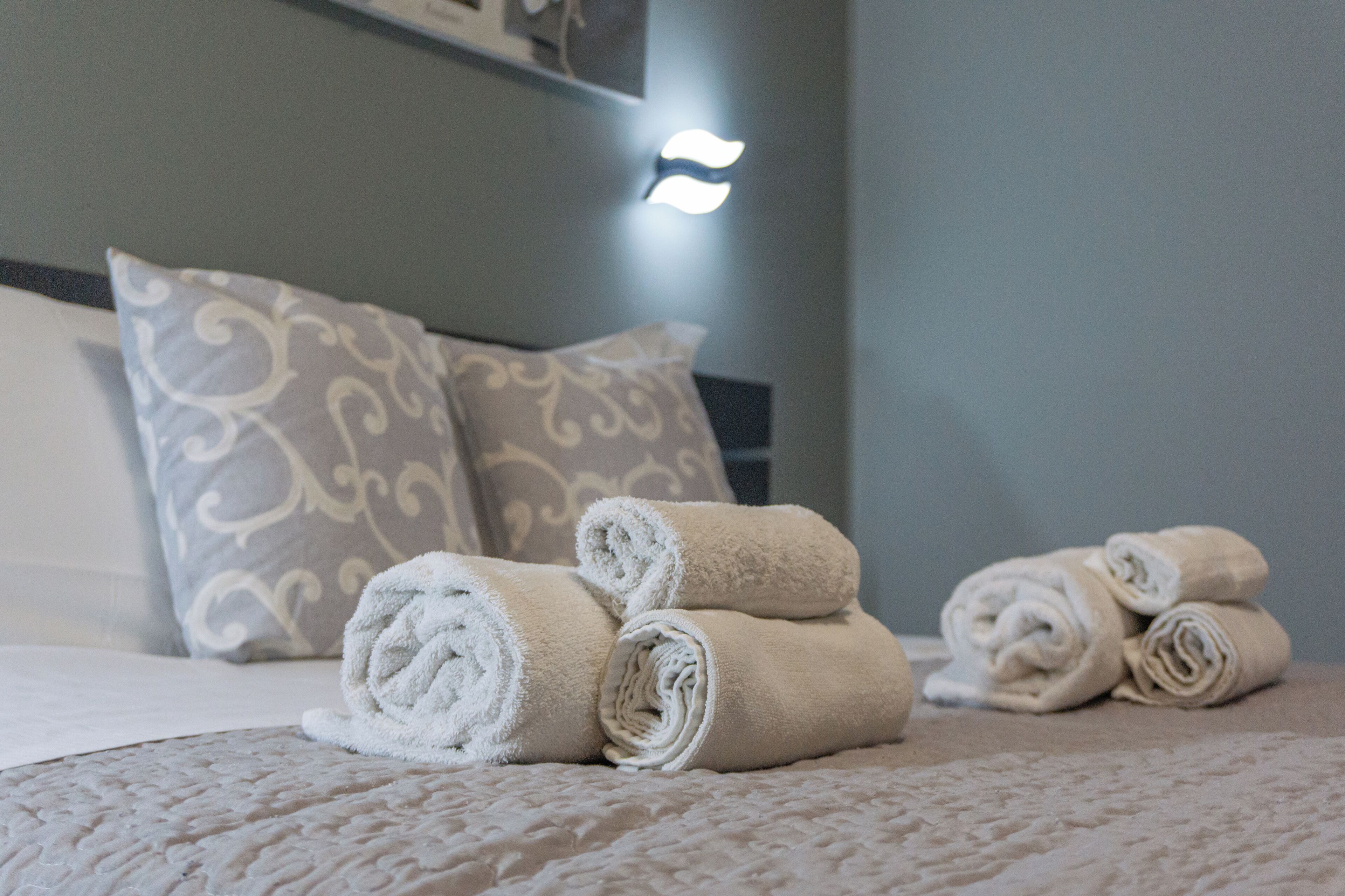 A neatly made bed with rolled towels and patterned pillows.