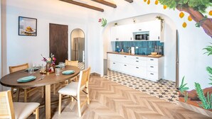 Un comedor con mesa y sillas de madera, una cocina con armarios blancos y salpicadero azul, y un suelo con estampado de espiga.