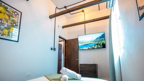 Habitación de hotel con una cama, un cuadro, un televisor y una puerta que da a otra habitación.