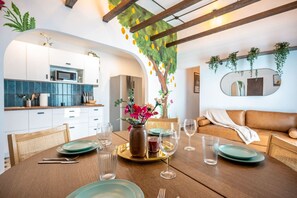 Un comedor con una mesa de madera preparada para cuatro personas, un florero con flores y una cocina al fondo.