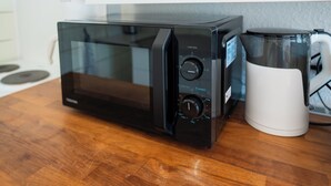 Eine schwarze Mikrowelle mit Timer und Auftau-Funktion auf einer Holzoberfläche neben einer weißen Tasse.