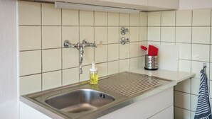 Eine Küche mit Spüle aus Edelstahl, einer Flasche Geschirrspülmittel und einem Metallbehälter mit einem roten Tuch.