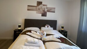 Una cama bien hecha con toallas dispuestas en forma de cisnes, una obra de arte en la pared encima y dos lámparas de noche sobre mesitas.