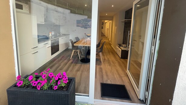 Una cocina moderna con armarios blancos, una mesa de comedor de madera y un felpudo negro en la entrada.