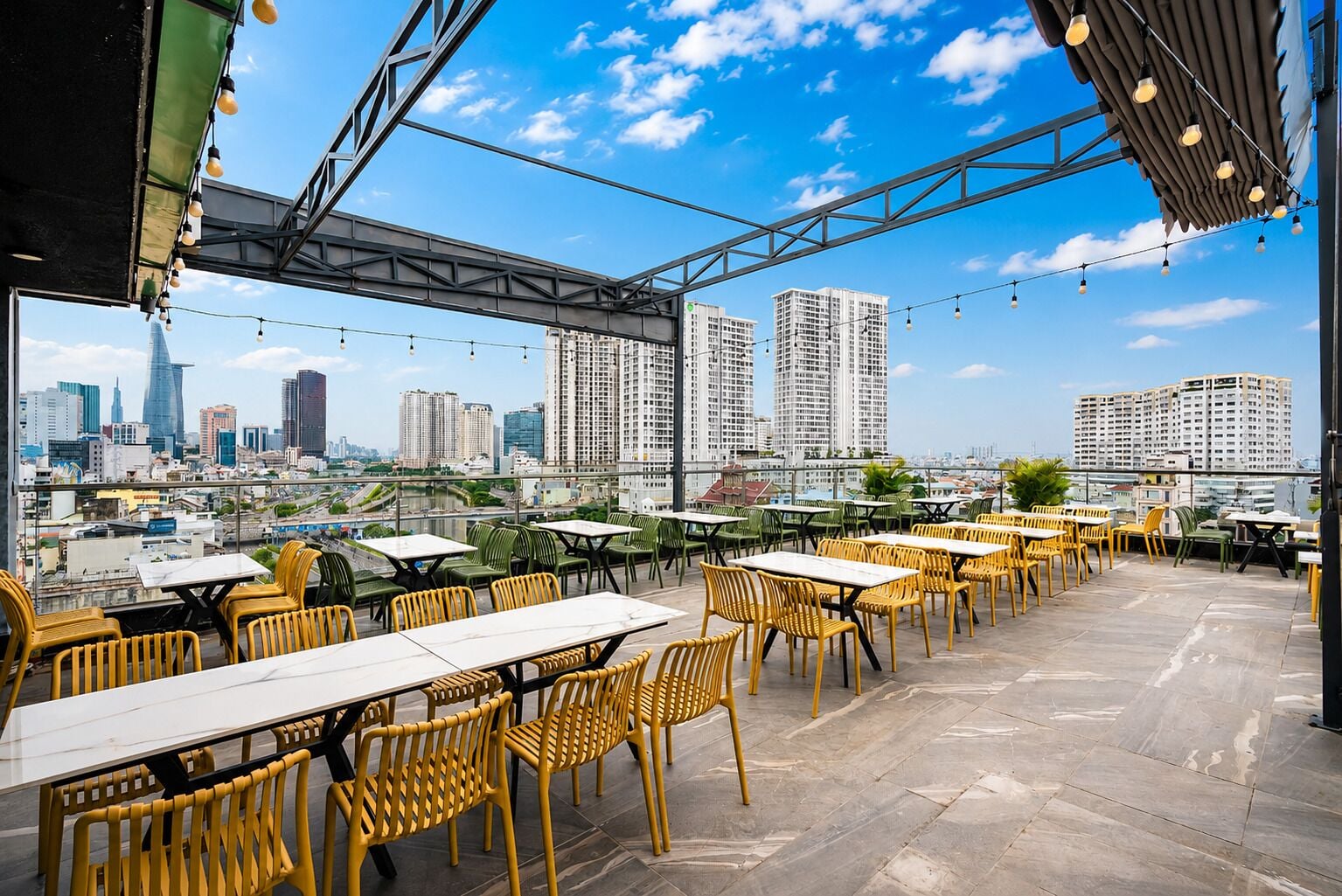 An outdoor dining area with tables and chairs, overlooking a cityscape with high-rise buildings.