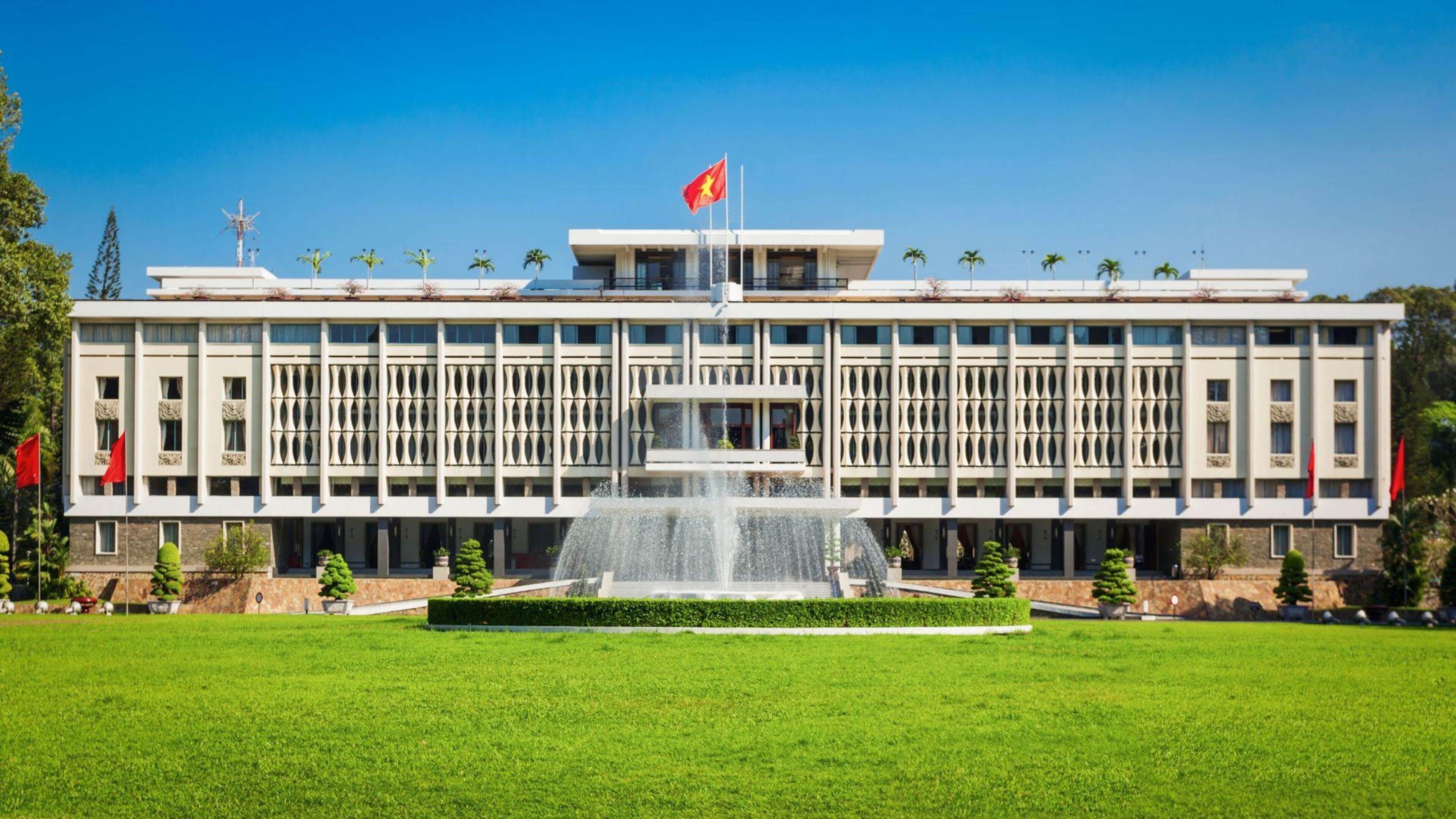 Un edificio grande con una fuente central, rodeado de un césped cuidado y palmeras.