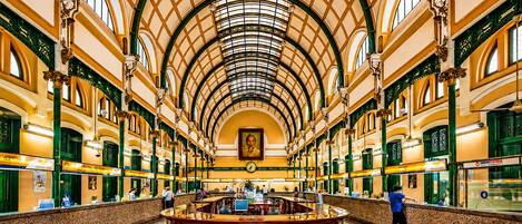 A spacious atrium with a high arched ceiling, a central information desk, and green-framed windows.