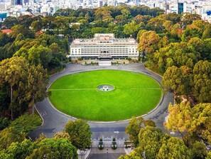 Un amplio espacio circular, con césped y una fuente central, rodeado por un camino y árboles.