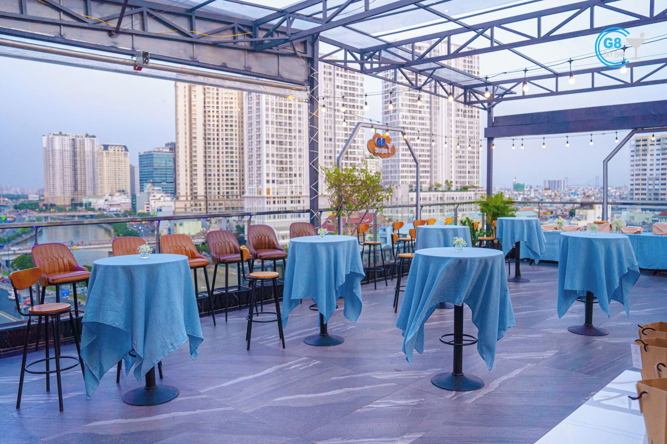 An outdoor dining area with tables and chairs, a view of the cityscape, and a sign for 'G8 Sky Bar'.