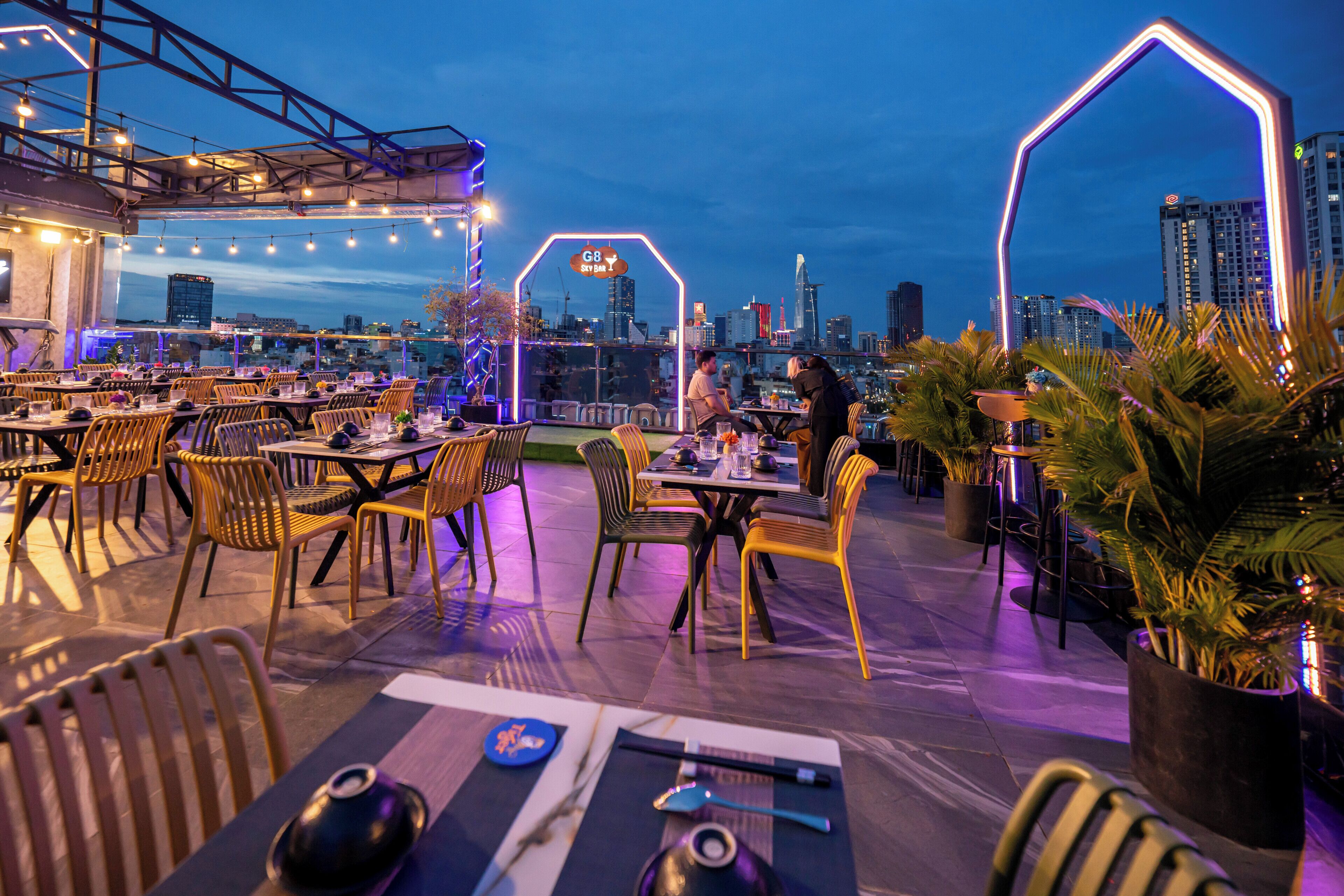 An outdoor dining area with tables and chairs, a city skyline in the background, and a sign for 'G8 Sky Bar'.