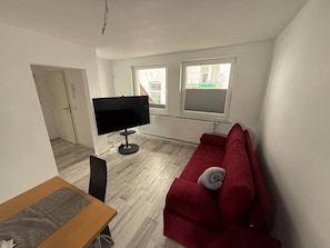 A living room with a red sofa, a TV on a stand, and a dining area with a table and chairs.
