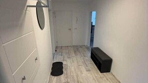 Una habitación con suelo de madera, un armario blanco, un banco negro y una puerta que da a otra habitación.