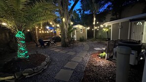 Un patio con baldosas de piedra, mobiliario exterior e iluminación con luces colgantes.