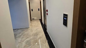 A modern hallway with a marble floor, a digital elevator control panel, and a door at the end.