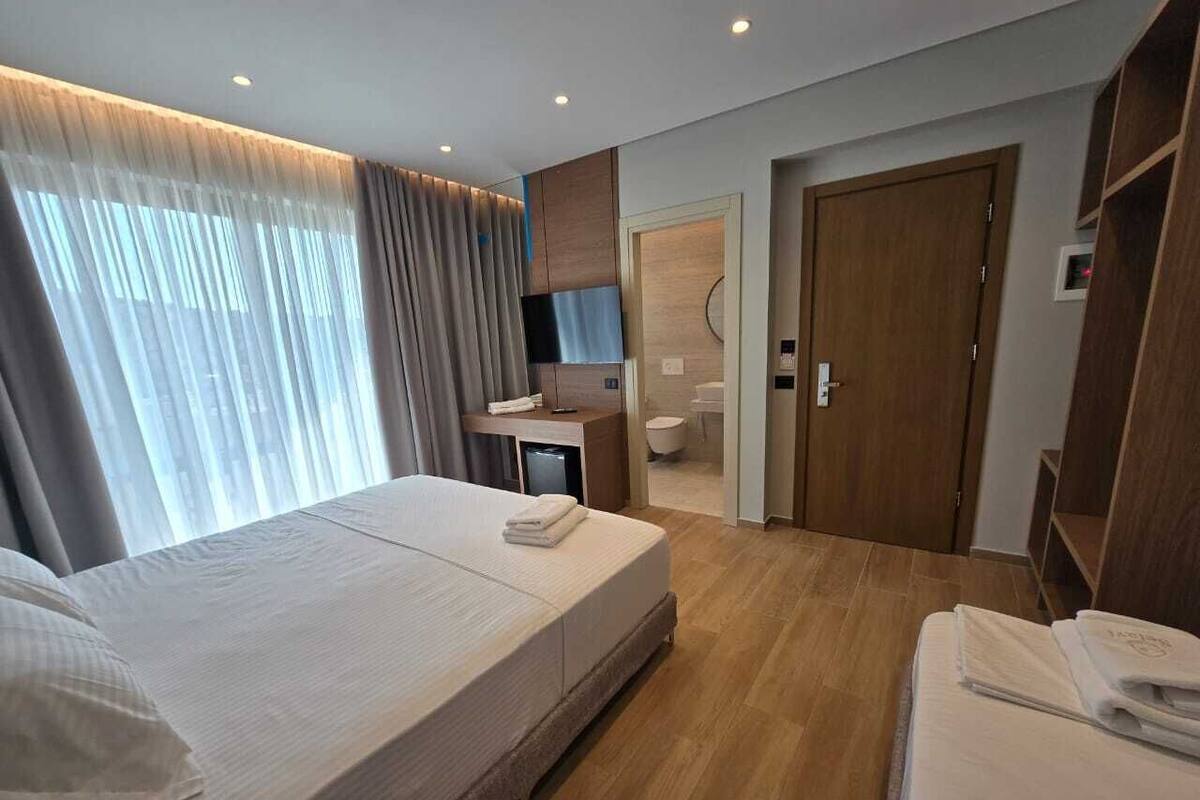 A modern hotel room with a large bed, a desk, a TV, and a bathroom visible through an open door.
