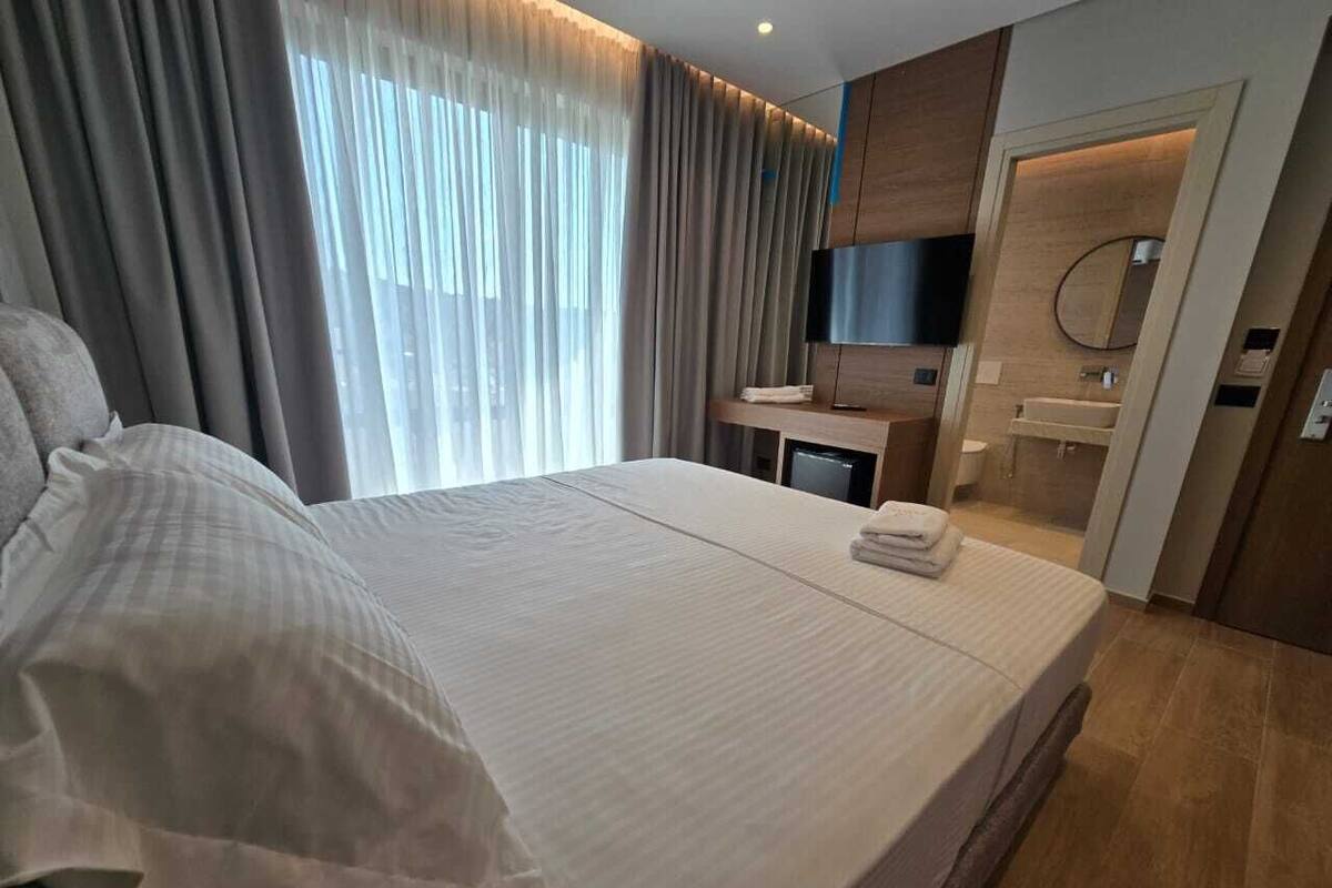 A modern hotel room with a large bed, a desk, a TV, and a bathroom.
