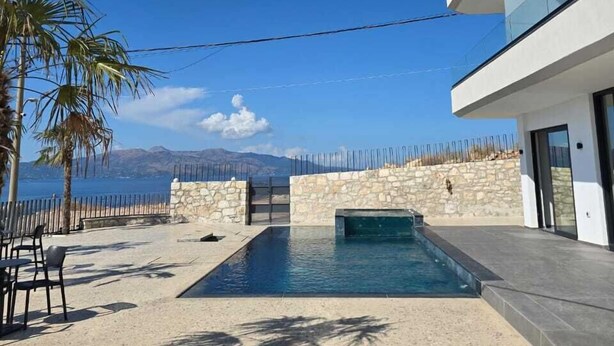 A modern building with a swimming pool, stone walls, and a view of the sea.