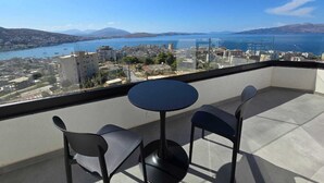 A balcony with a round table and two chairs, overlooking a cityscape with buildings and a body of water.