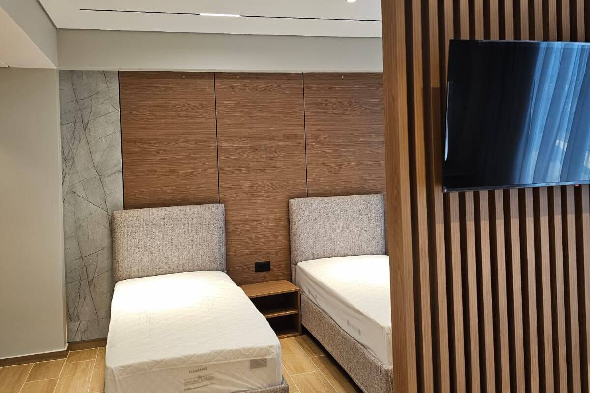 A modern bedroom with two beds, a wooden headboard, a TV mounted on a wooden panel, and a marble accent wall.