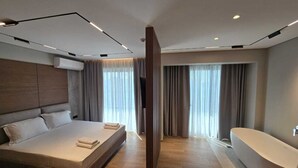 A modern hotel room with a large bed, a separate bathroom, and a large window with curtains.