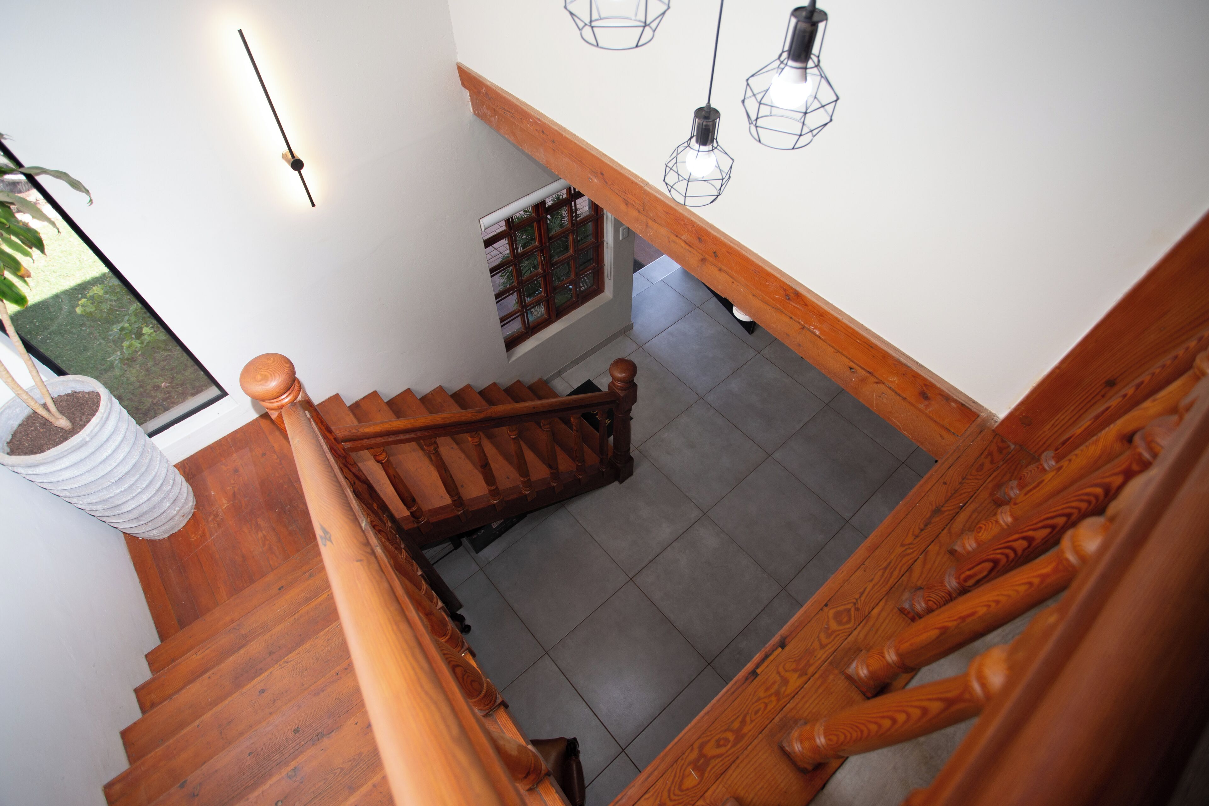 Una escalera de madera con barandilla, una planta en maceta y lámparas colgantes.