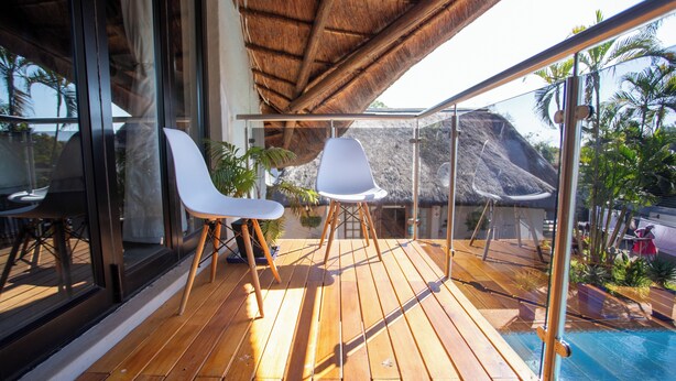A wooden deck with two white chairs and a glass balustrade overlooking a pool and tropical scenery. - Golden Casa (Mokopane)