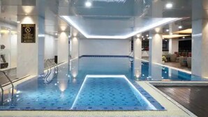 An indoor swimming pool with a blue tiled floor, a central light fixture, and a sign on the wall. - Hotel Horison Ultima Entrop (Jayapura)