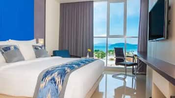 A modern hotel room with a large bed, a desk, and a view of the sea.