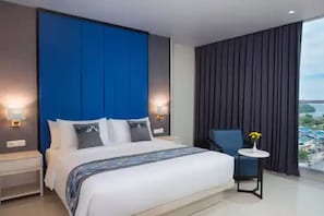 A modern hotel room with a large bed, a blue accent wall, a view of the sea, and a small table with a vase of flowers. - Hotel Horison Ultima Entrop (Jayapura)